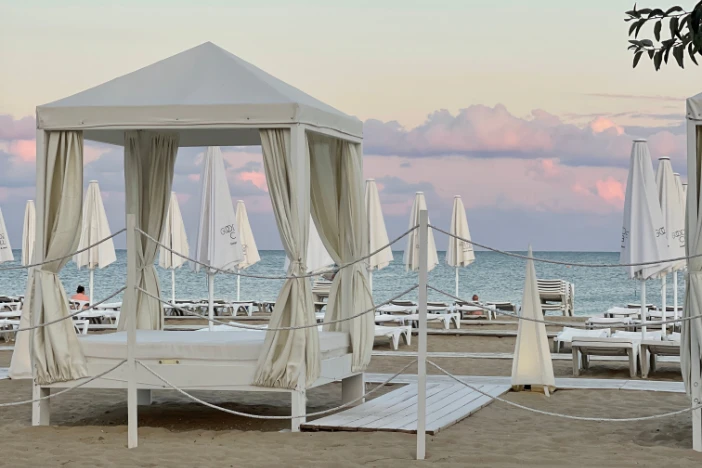 White cabana with tied-back curtains on a beach with closed umbrellas and loungers in the early morning