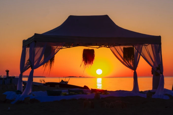 Silhouette of a basic canopy with sheer curtains on a beach at sunset