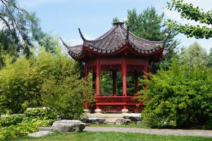 Red Asian-style octagonal pavilion with an ornate curvaceous black roof in a green garden near a path