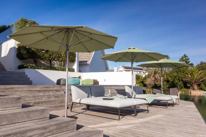 Three market umbrellas with light green canopies shade off white sun loungers on a hardwood deck under a clear blue sky