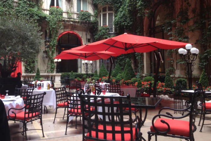 Black Tuscan-style metal dining chairs with red seat cushions around tables with cantilever umbrellas at an outdoor cafe