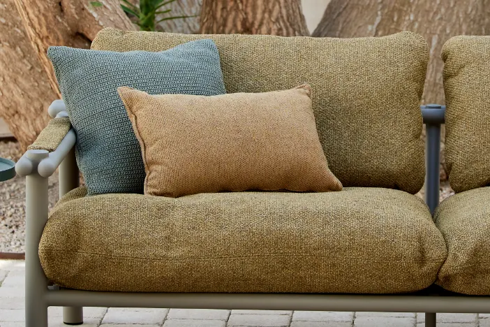 Plush olive green upholstered outdoor sofa with rust and teal accent pillows on a brick patio