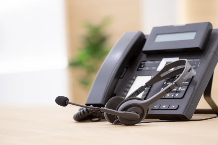 Black landline office phone with modern headset sitting on a light tan table