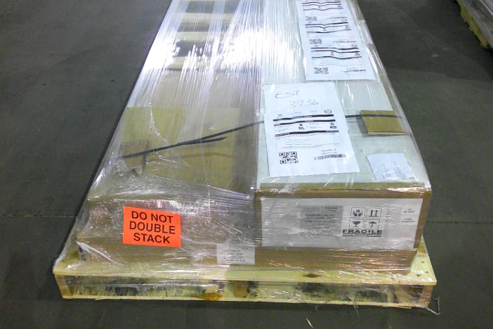 Long package with white labels shrink-wrapped on a wooden pallet in a warehouse