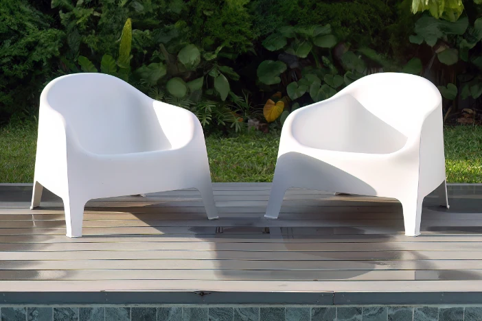 Two minimalist modern white molded plastic outdoor lounge chairs on a poolside deck