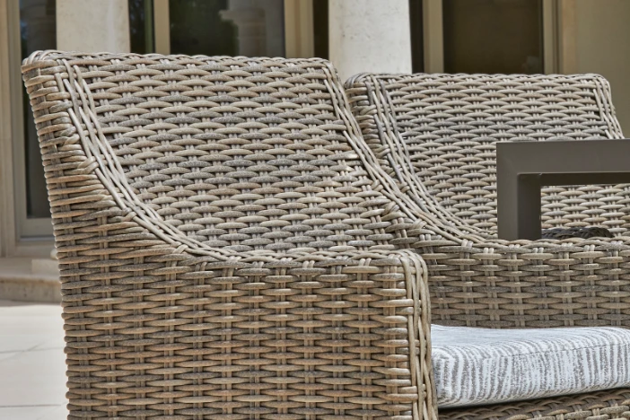 Two medium brown all-weather wicker dining armchairs with thin grey seat cushions