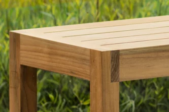 Close-up view of the corner of a teak wood bench with slats in a grassy area