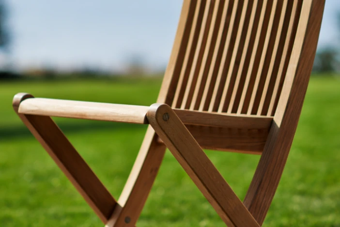 Low angle view of a folding side chair made of teak slats in a bright green grassy field