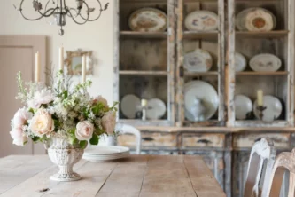 Shabby chic dining room with plain wood table and chair with weathered cupboard showcasing dishes in the back