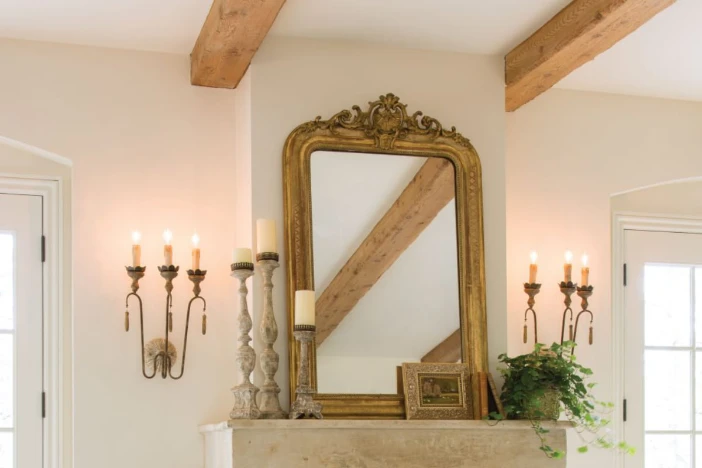 Ornate mirror with a gold leaf frame with weathered candlesticks and flanked by candelabra style shabby chic sconces on either side