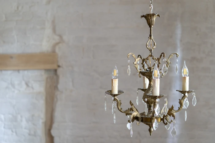 Small vintage brass chandelier with decorative crystal droplets in front of a white distressed brick wall