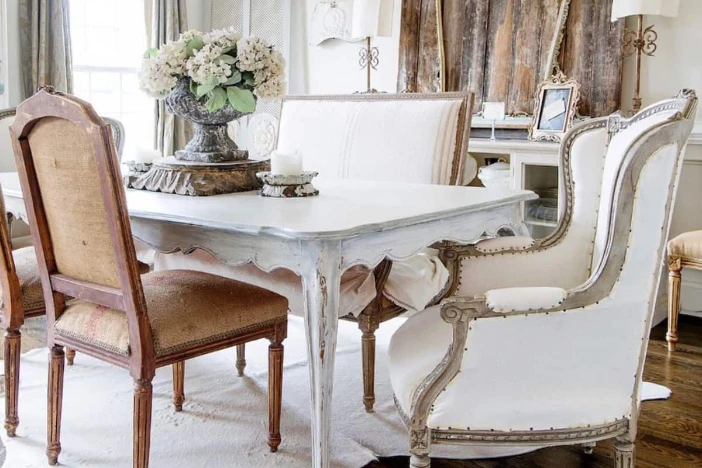 White distressed rectangular dining table surrounded by an eclectic mix of upholstered armchairs and side chairs with aged wood frames