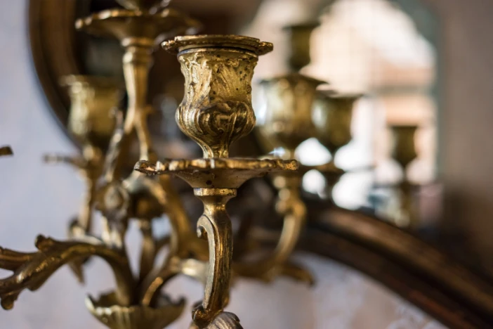 Detailed view of antique chandelier with aged gilded gold finish in front of a mirror