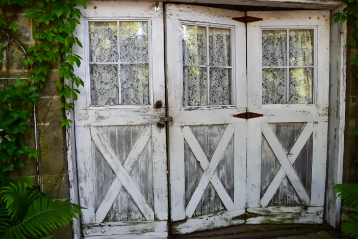 Farmhouse styled doored with distressed white finish and lacy curtains behind window panes