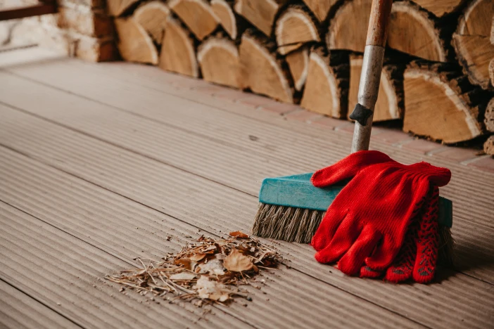 Deck with swept leaves and debris next to a broom with red glove near a stack of firewood