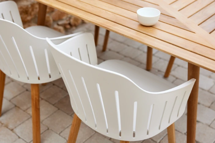 White recycled plastic outdoor dining chairs with teak legs next to a wooden table