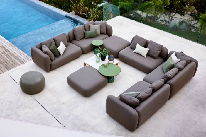 Outdoor modular sofa with chocolate brown upholstery and accent pillows on a poolside patio