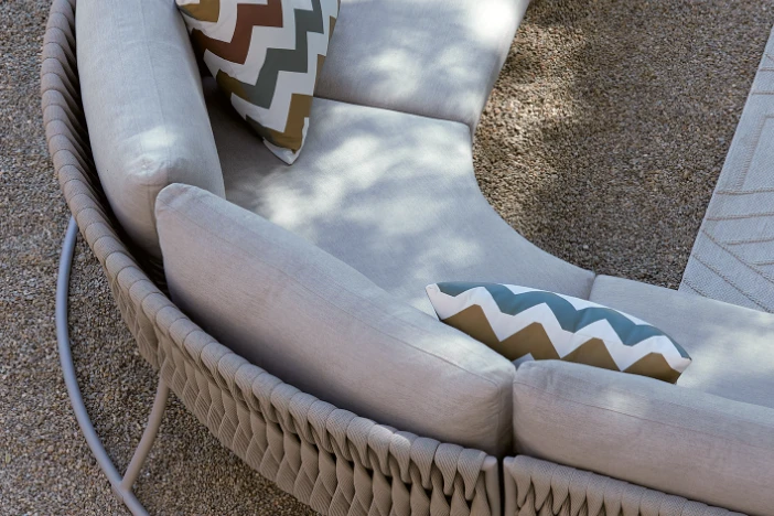 Curved outdoor sectional sofa with greyish brown weave and upholstery with muted green and umber zig-zag striped pillows