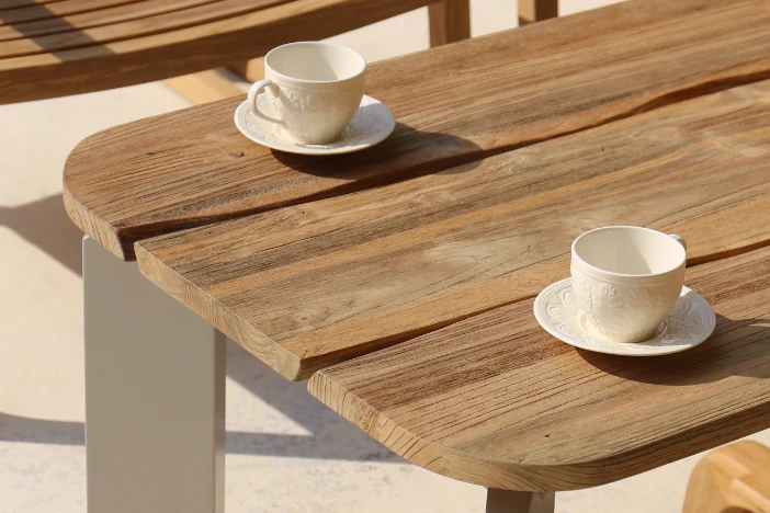 Close-up of an outdoor coffee table with a recycle teak top and metal legs with two cream colored coffee cups