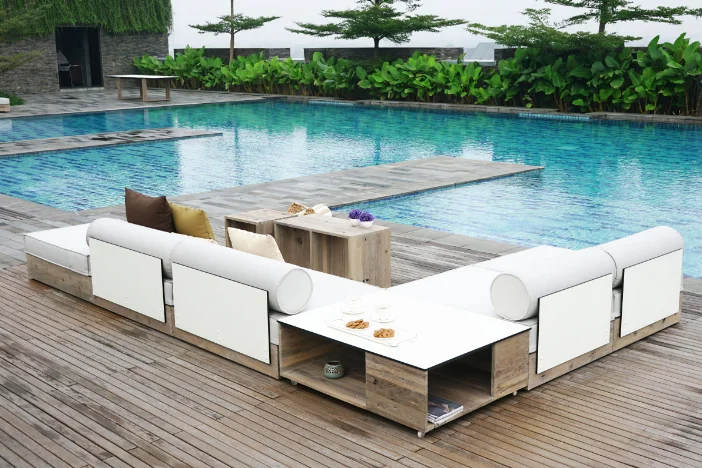 Outdoor recycled teak sectional sofa with modular mobile coffee tables on a hardwood deck around a tiled pool