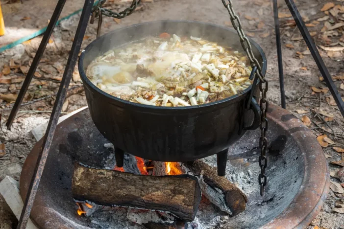 Suspended cauldron with stew cooking over an open wood-burning fire pit