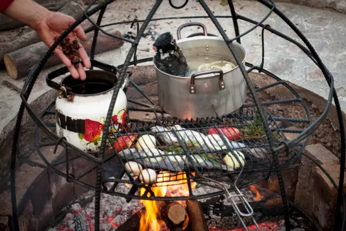 Stone fire pit with fish, stew and vegetables cooking on a permanent multi-level grill