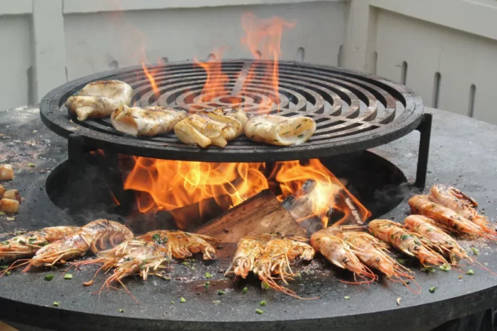 Round plancha fire pit with shrimp cooking on the outer griddle andcalimari on an elevated central grill