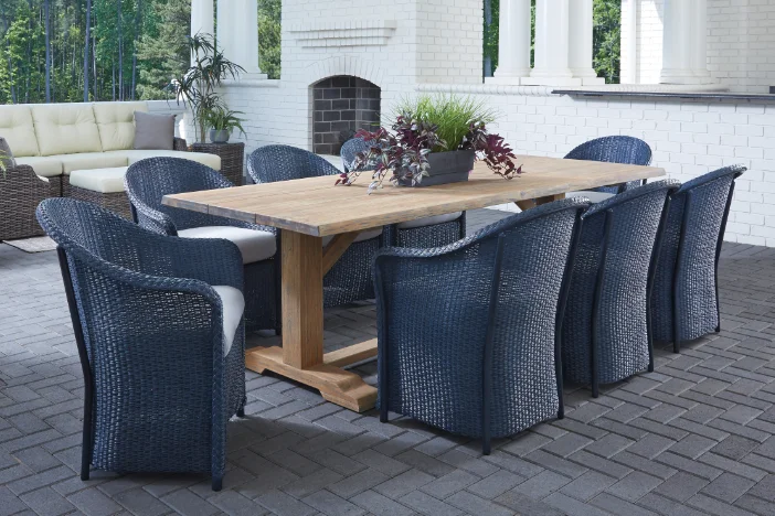 Slim black wicker armchairs with white seat cushions around a rectangular wooden dining table on a grey brick patio