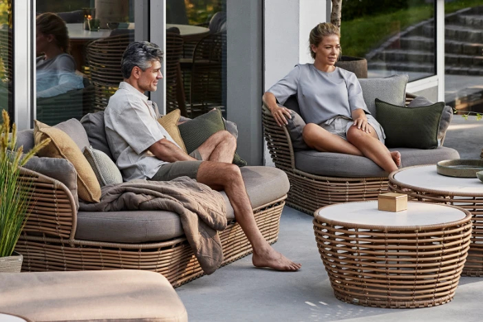 Man and woman sitting on modern brown rattan lounge seating with mocha cushions on a patio