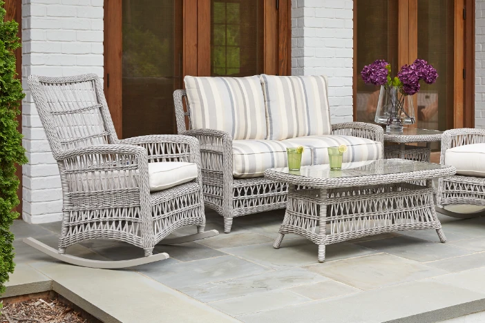 Grey wicker rocking chair and loveseat with striped cushions surrounding a matching coffee table on a small porch