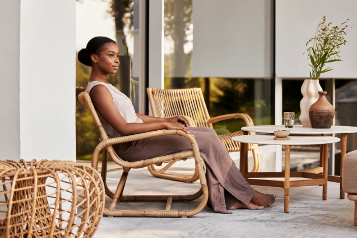 Woman sitting in a rattan outdoor armchair with other lounge furniture on a patio