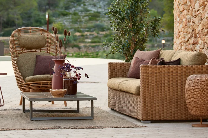 Light brown rattan outdoor lounge chair and wicker loveseat with olive green upholstery on a patio