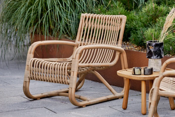 Light brown rattan arm chair next to a wooden side table on a paver patio