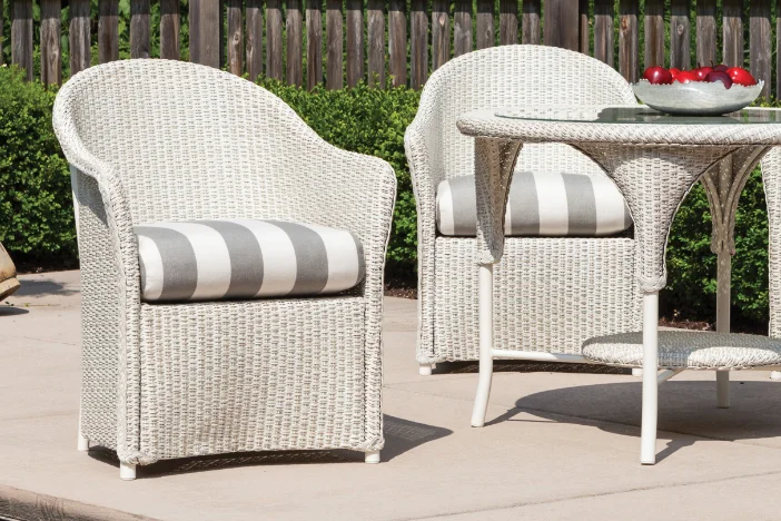 Two white wicker arm chairs with light grey striped seat cushions on a concrete patio with a matching round table