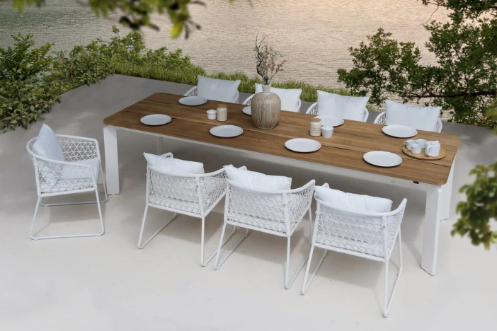 Rectangular outdoor dining table with white base and teak top surrounded by white rope dining chairs