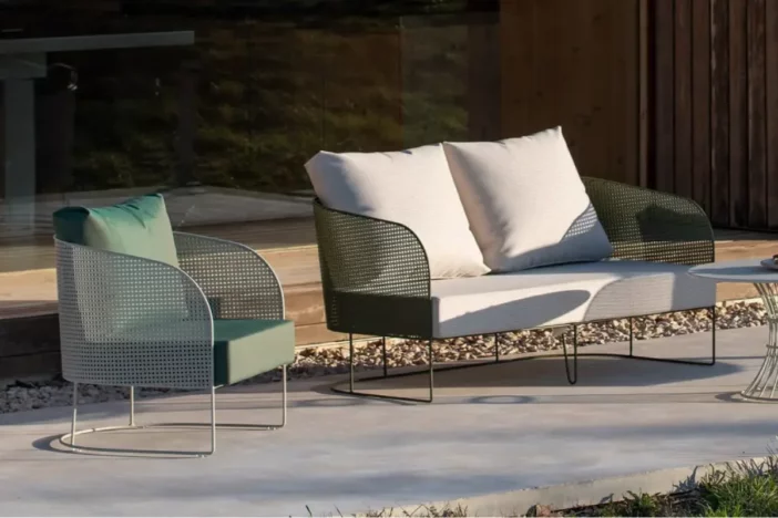 Light green aluminum lounge chair and loveseat with perforated wraparound bodies and plush cushions on a patio