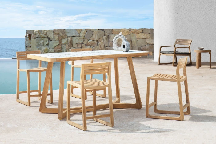 Teak counter stools with slatted seat and backrests around a matching rectangular table with a white HPL top sitting poolside