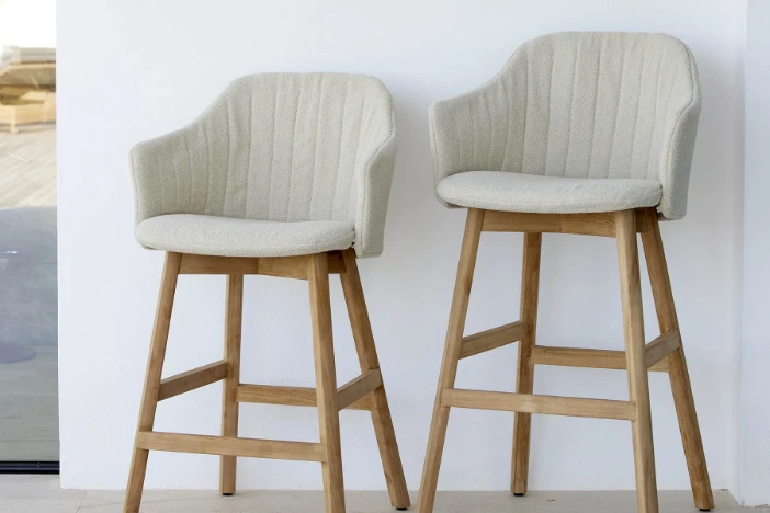 Two counter and bar height outdoor stools with flared wooden frames and off-white upholstered bodies