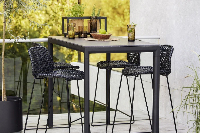 Black outdoor wicker barstools with wireframes at a dark grey bar table with iced drinks on a terrace