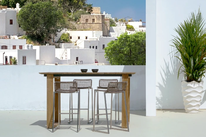 Slender bars stools with taupe woven seat and backrests and metal frames at a teak bar table with a beautiful vista in the background