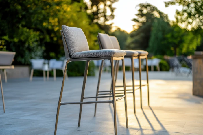 Three light grey upholstered counter stools with slender metal frames on a spacious patio near trees