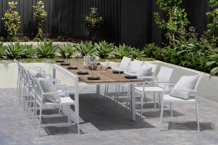 Modern white metal dining table with a teak top and matching chairs on a low walled patio