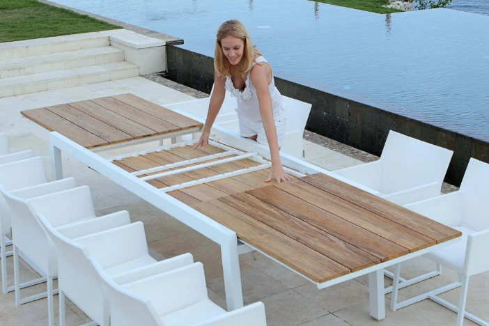 Woman accessing drop leafs of a long dining table with a teak top and white metal frame