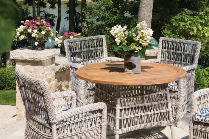 Small round patio dining table with a wooden top and grey wicker base with matching armchairs