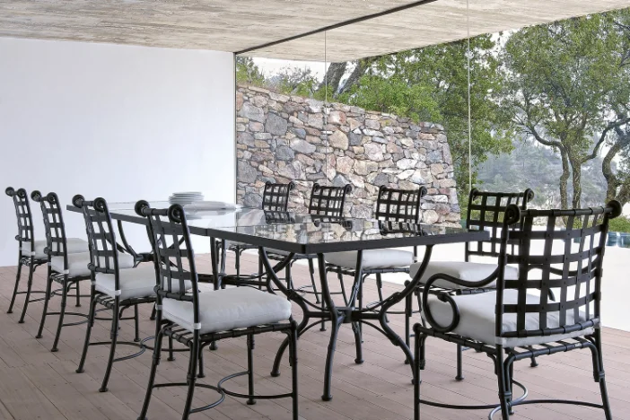 Tuscan style black metal chairs around a matching rectangular table with a clear glass tabletop in a sunroom