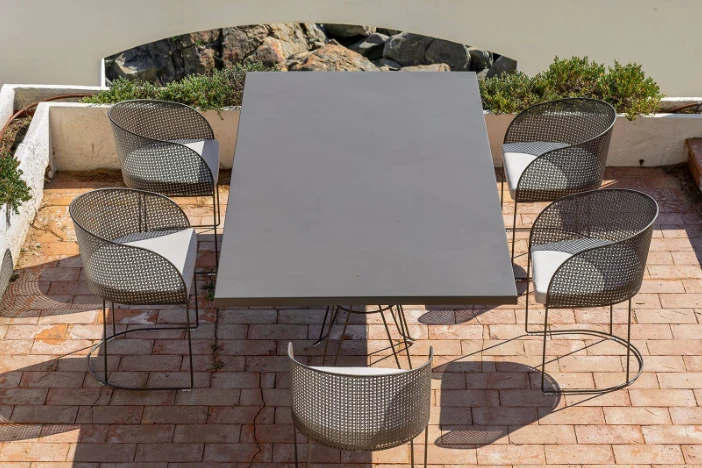 Bronze metal rectangular table and rounded mesh bodied chairs with white seat cushions on a brick patio