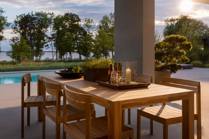 Rectangular wooden dining table with matching chairs near an outdoor swimming pool