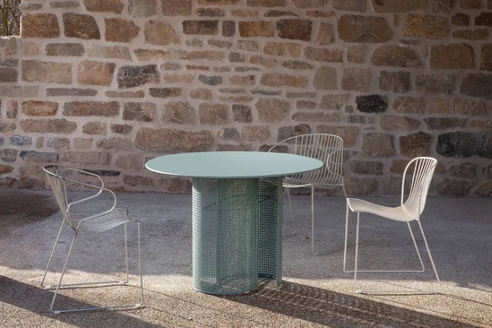 Sea foam green round metal table with perforated base and white wireframe chairs