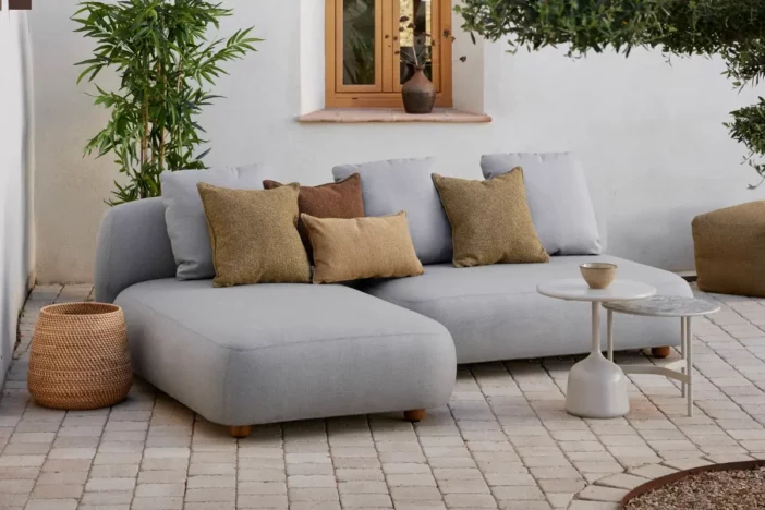 Plush grey sectional chaise with brown pillows and round side tables