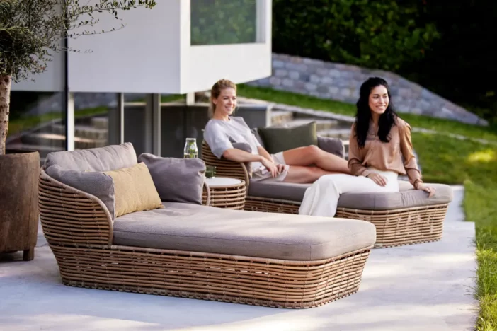 Women sitting on brown rattan armed chaises with taupe cushions on a patio